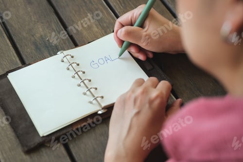 Preview: woman writing goal on notebook at coffee shop outdoor space