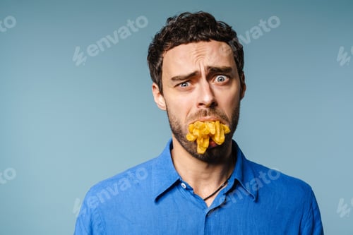 Preview: Unhappy handsome guy posing with french fries in his mouth