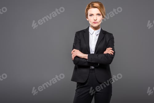 Preview: serious businesswoman posing in suit with crossed arms, isolated on grey