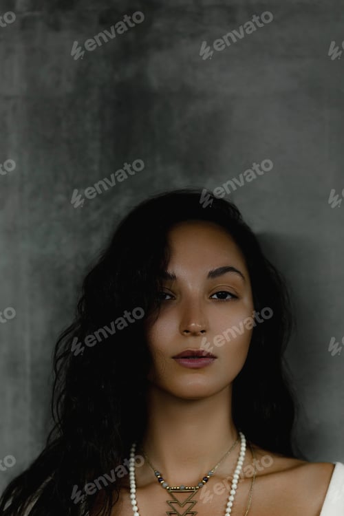 Preview: Young caucasian female with long dark hair and beaded necklace against gray background
