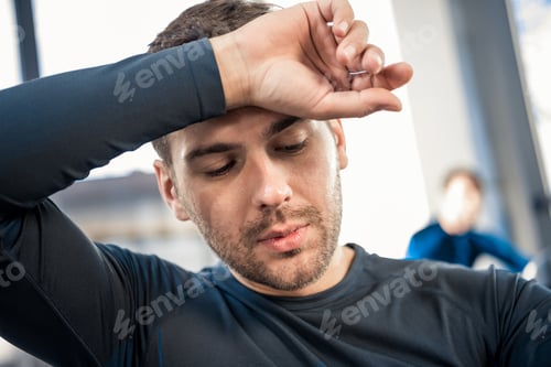Preview: Tired young man wiping face by hand at gym
