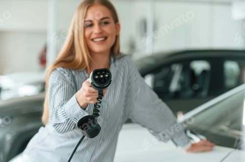 Preview: Holding charger for electric car. Beautiful woman is indoors