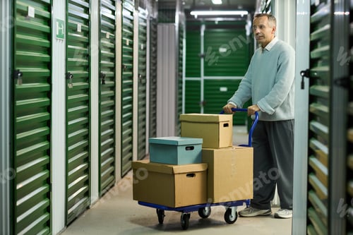 Preview: Middle Aged Man Maneuvering Cart Loaded with Boxes in Storage Hall