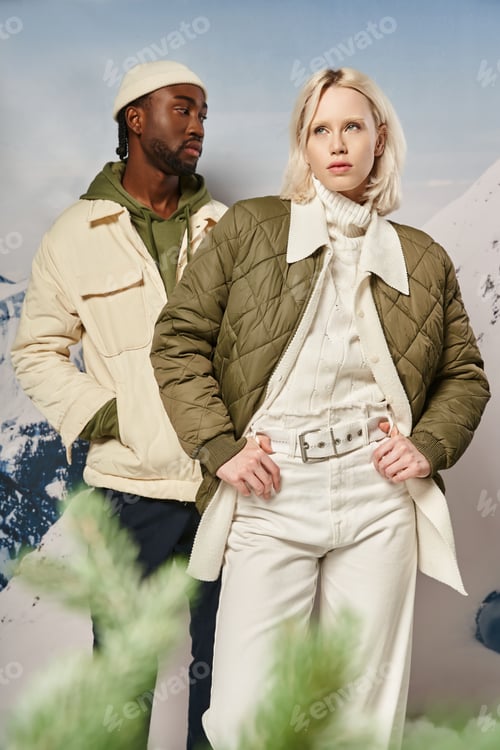 Preview: attractive stylish couple in warm clothes posing next to fir tree with mountain backdrop, winter