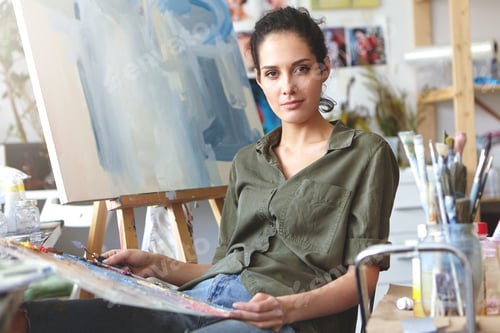 Preview: Picture of attractive professional young Caucasian female in casual clothes holding palette and pain