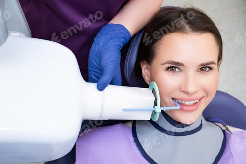 Preview: A dental assistant readies a patient for an X-ray procedure using specialized tools in the clinic.