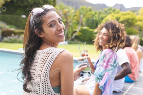 Preview: Young biracial woman smiles at the camera, friends enjoy drinks by the pool