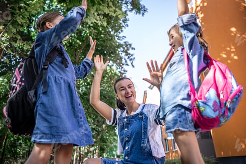Preview: Cheerful young mother and little daughters with backpacks before school lessons.