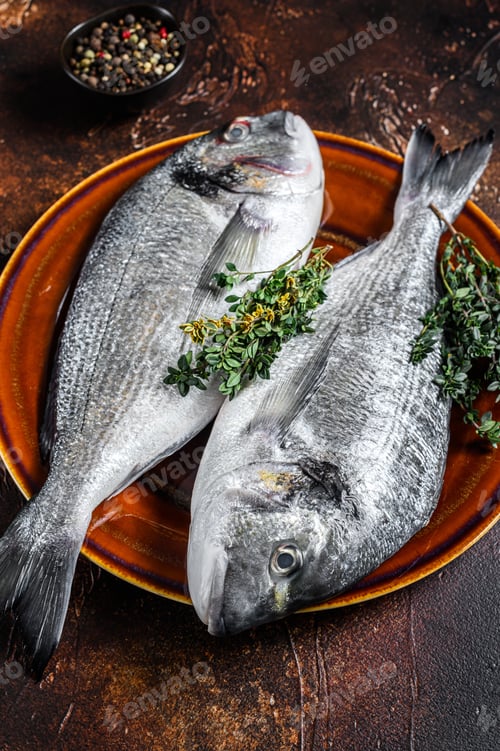 Preview: Raw Sea bream fish and ingredients for cooking. Dark background. Top view