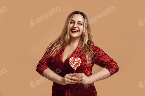 Preview: I love you. Plus size happy woman in velour dress holding a red heart-shaped lollipop and looking at