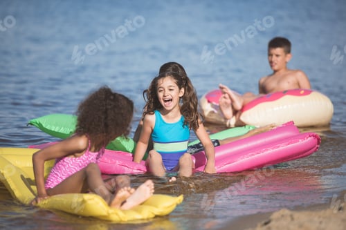 Preview: happy little kids have fun on inflatable mattresses at seaside