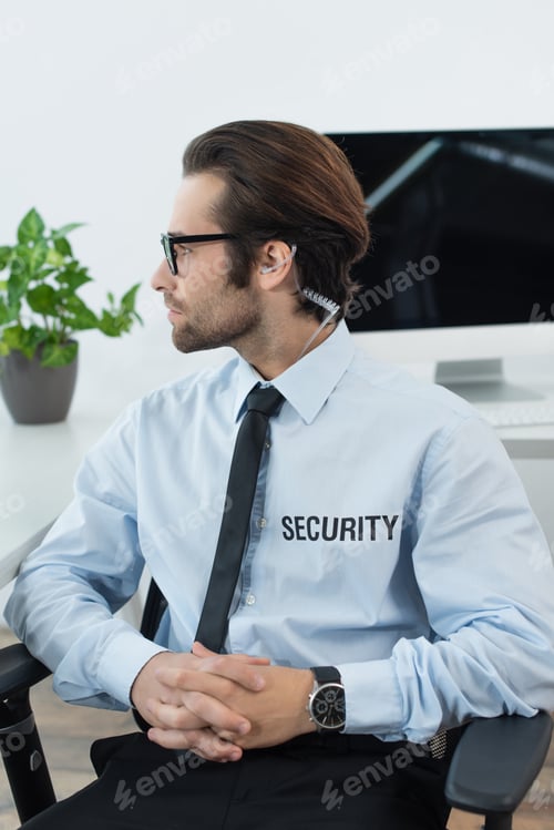 Preview: security man in earphone and eyeglasses sitting with clasped hands and looking away