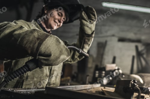 Preview: selective focus of female welder in protective work wear working in workshop