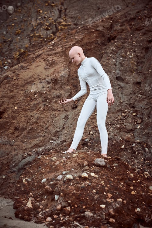 Preview: Full length portrait of young hairless girl with alopecia in white suit holding handful of earth