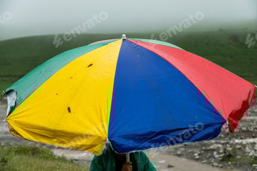 Preview: Man holding colorful beach umbrella during rain