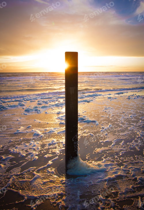Preview: Beautiful shot of a sunset in Dutch Island of Texel beach with beach pole and foam on the sand