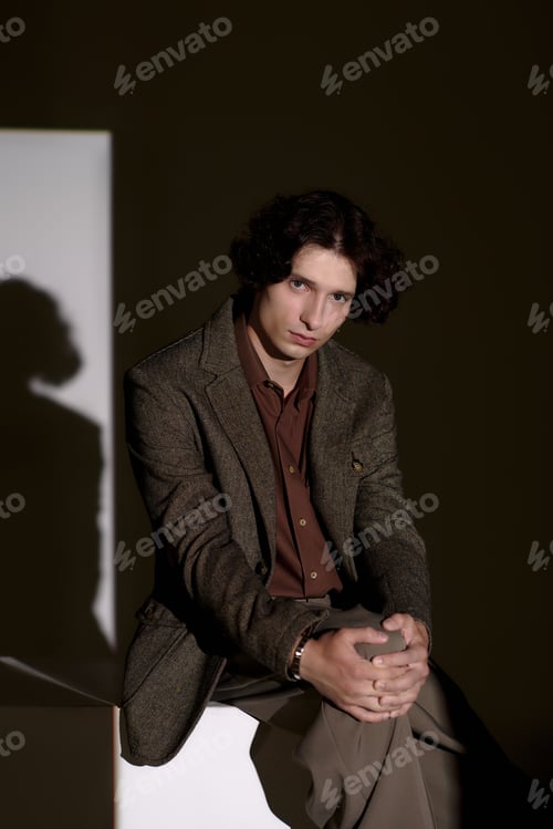 Preview: Stylish young man showcases unique fashion in sleek grey studio setting