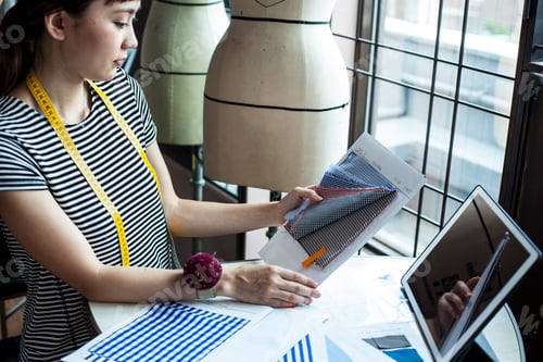 Preview: Japanese female fashion designer working in her studio, sitting at table, looking at fabric samples.
