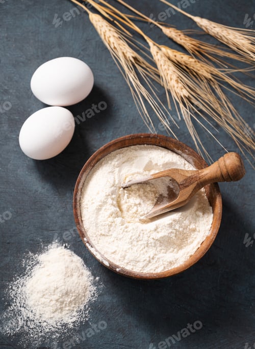 Preview: Wheat flour in a wooden bowl with a scoop on a dark blue background with eggs and dry branches wheat