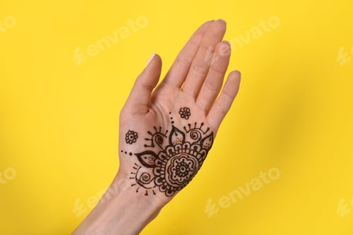 Preview: Woman with henna tattoo on palm against yellow background, closeup. Traditional mehndi ornament
