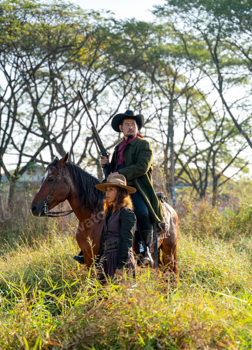 Preview: Young Asian woman with cowgirl costume stand in front of cowboy on horse with holding gun