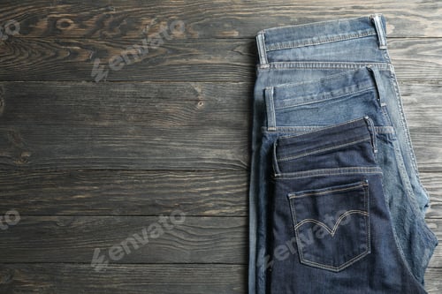 Preview: Different jeans folded on a wooden background, space for text