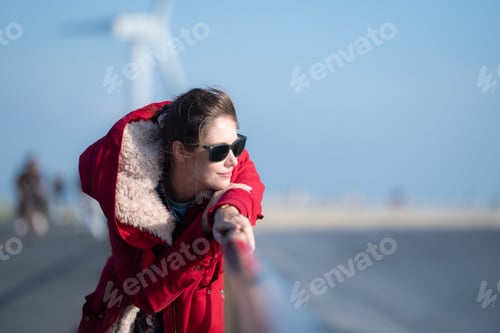 Preview: On the background of windmills, A young woman in a red jacket is enjoying her winter vacation.
