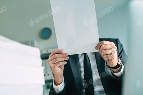 Preview: Unrecognizable business person holding blank white mockup paper in front of his face