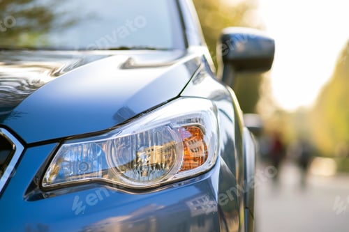 Preview: Closeup of front headlight of new clean car parked on a city street side