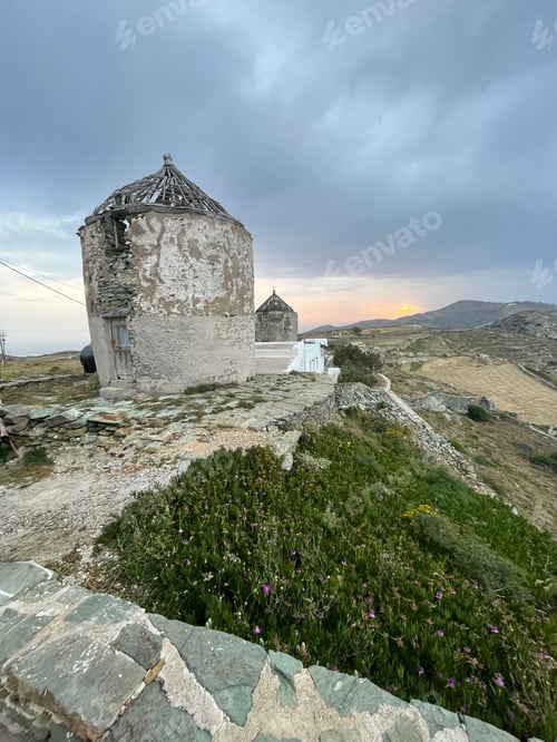 Preview: A scenic view of two windmills and a valley at dusk against a crooked hand built stone wall at dusk.