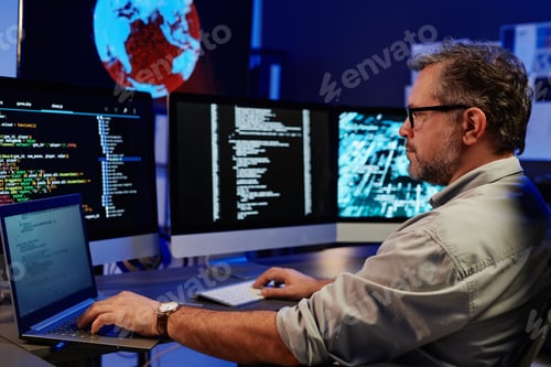 Preview: Side view of serious server engineer using laptop and computers