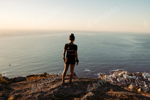 Preview: Back view of a woman looking down from the top of the mountain at sunset