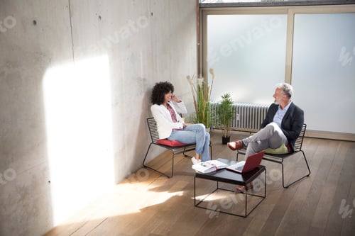 Preview: Businessman and businesswoman sitting in a loft at concrete wall talking