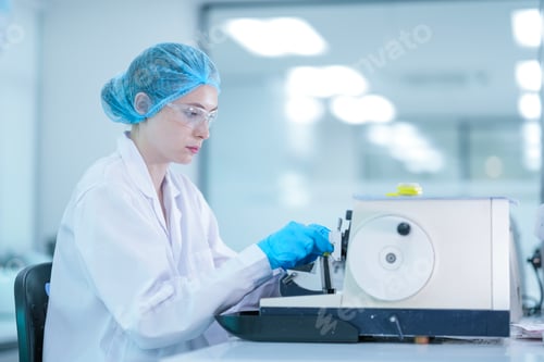Preview: A female scientist in a lab coat and hair net carefully works with a medical machine