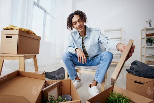 Preview: guy with curly hair unpacking things from boxes in the room Lifestyle