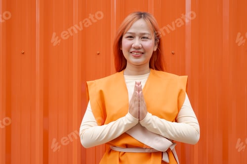 Preview: Beautiful Thai Woman Making Traditional Wai Sawasdee Greeting Against Orange Background