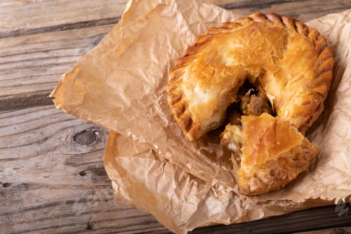 Preview: High angle close-up of sliced baked stuffed pie in brown wax paper on wooden table