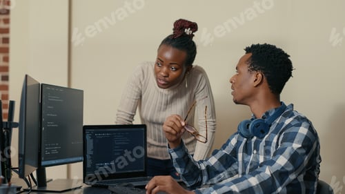 Preview: Database developer removing glasses while explaining algorithm to colleague coder pointing at