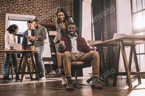 Preview: multiethnic casual business couple using smartphone with colleagues working in modern loft office