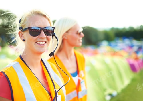 Preview: Two young female security assistants standing on a campsite at an outdoor music festival