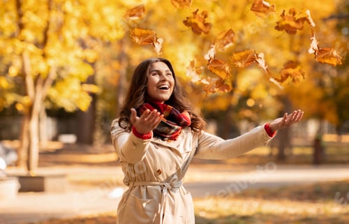Preview: Joyful young woman in autumn outfit catching yellow leaves during her walk at park on bright fall