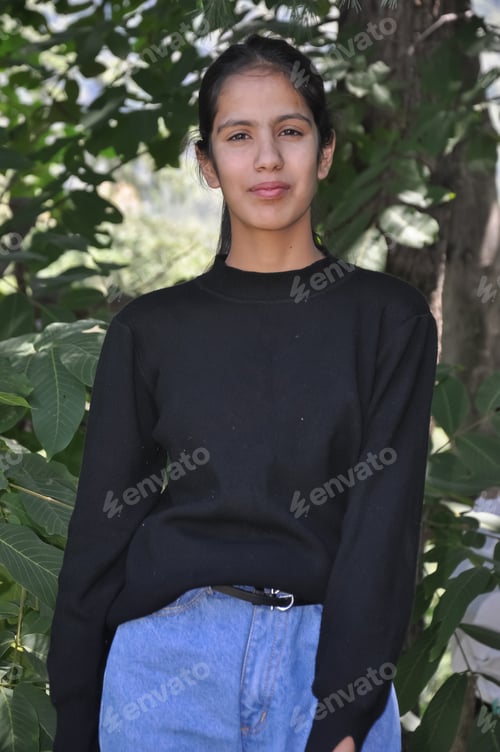 Preview: Portrait of a lovely young girl wearing casual clothes standing against leafy tree
