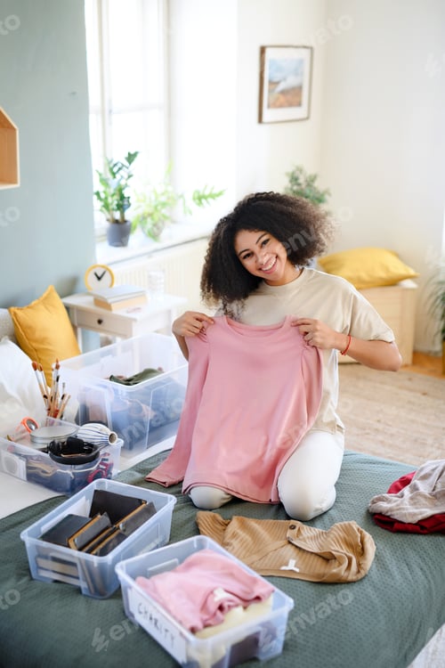 Preview: Young woman sorting wardrobe indoors at home, charity donation concept.