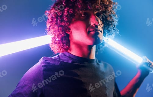 Preview: Young beautiful man with curly hair is indoors in the studio with neon lighting