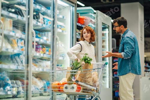 Preview: Couple discussing groceries shopping in supermarket refrigerator aisle