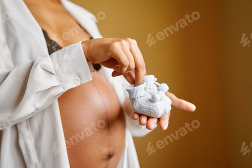 Preview: pregnant african woman holding baby socks with her hand on her belly