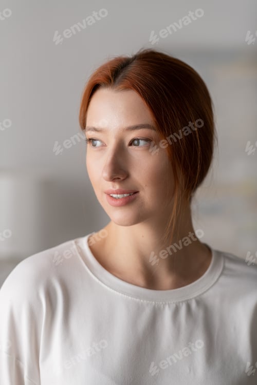 Preview: Young woman with vibrant red hair enjoying a peaceful moment in her modern apartment