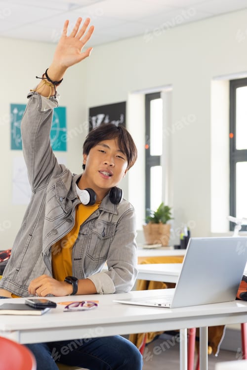 Preview: In school, asian teenage boy raising hand while sitting at desk with laptop