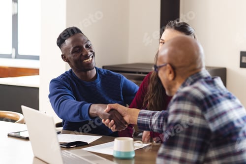 Preview: Diverse couple and biracial male financial advisor using laptop and shaking hands at home