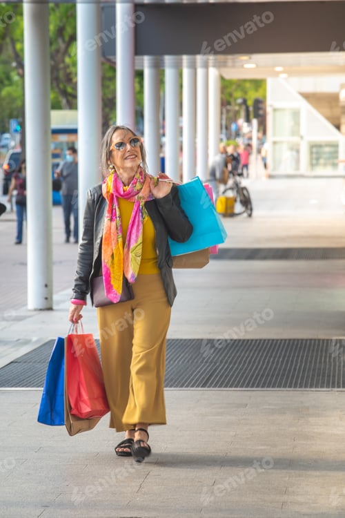 Preview: Happy senior attractive lady with shopping bags walking in the street smiling. Festive shopping sale
